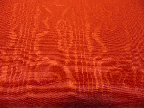 A worsted baize, embossed with a black moire. This is a drapery and upholstery fabric in a deep, rich cinnabar.
