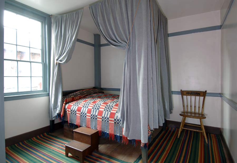 Simple bed hanging in two color m's and o's pattern in cotton
and linen at the Farmers' Museum in Cooperstown, NY.